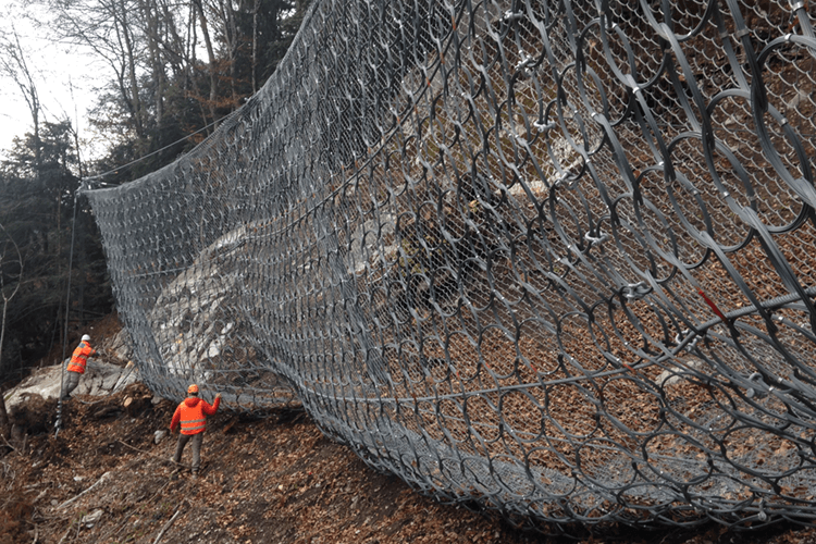 Des ingénieurs portant des vestes de sécurité orange inspectant un très grand filet anti-chute de pierre en automne en montagne