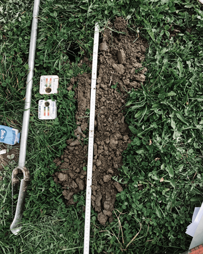 Un double-mètres et divers instruments de mesure posés sur de l'herbe, avec de la terre retournée sous le double-mètre au centre de l'image.