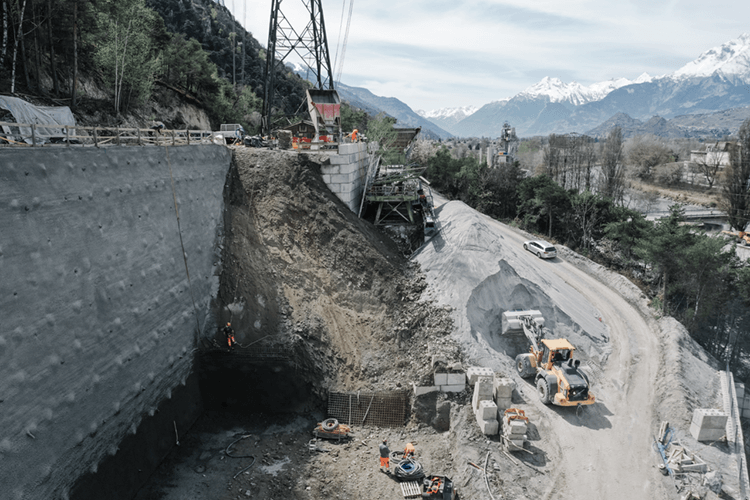 Des machines à l'oeuvre sur un chanter alpin avec la construction d'un grand mur de sécurité sur la gauche de la photo.