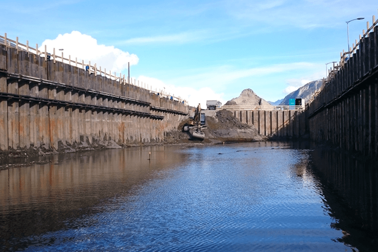 Une pelle mécanique à l'oeuvre dans un grand bassin en chantier entouré de murs métalliques.