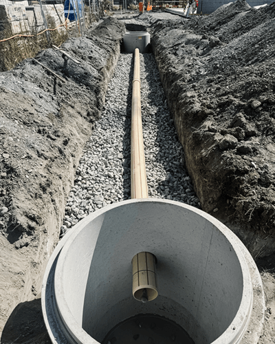 Des canalisations en cours de constructions, avec 2 cercles en béton sur lesquels iront des grilles reliés par un grand tuyau en plastic dans une tranchée.