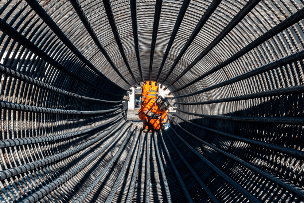 Une personne portant un uniforme de travail orange vif vue au travers d'un ensemble de câbles en métal.