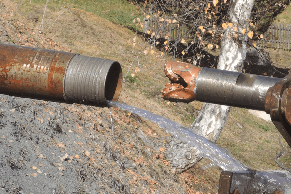 Un grand tuyau mécanique sur la gauche d'où s'écoule de l'eau et une foreuse mécanique sur la droite qui est destinée à entrer dans le tuyau pour forer.